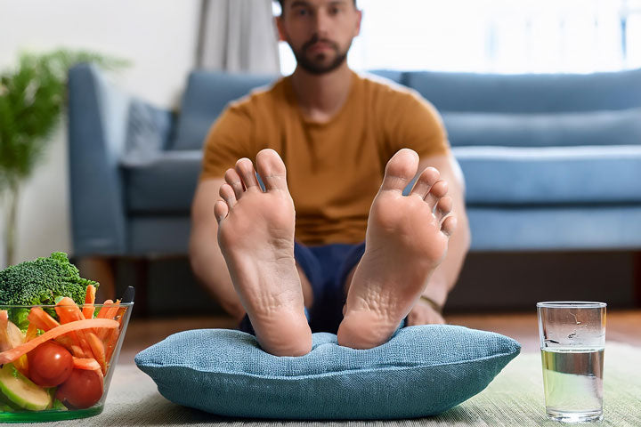Adult male elevating a swollen ankle on a pillow at home, showing how to reduce ankle swelling with rest and elevation